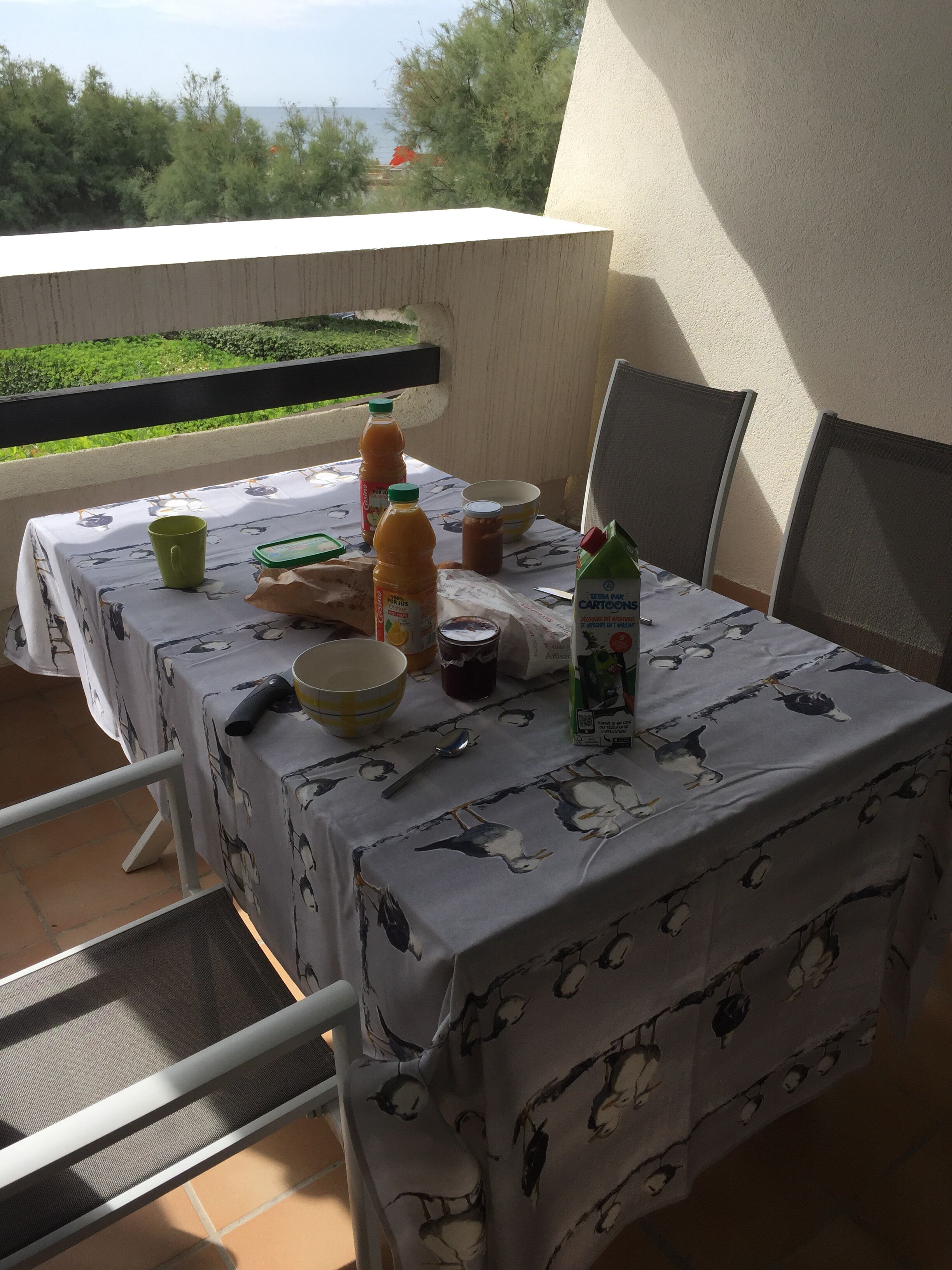 A table set on a balcony with a tablecloth featuring bird patterns, various food items, and condiments.