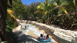Un toboggan aquatique où des personnes dévalent la pente à l’intérieur de bouées gonflables, le tout entouré d’une végétation tropicale.