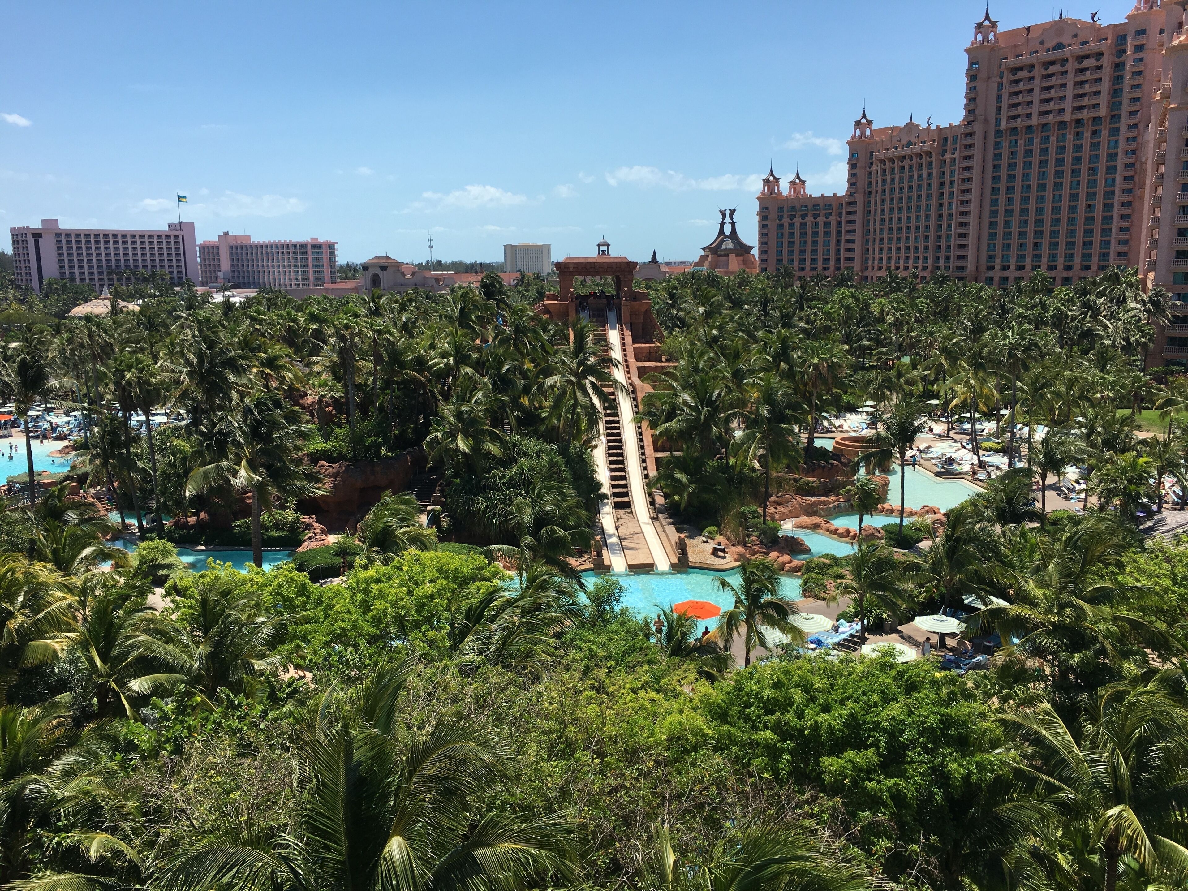 Un complexe hôtelier doté de plusieurs piscines, de palmiers et d’un toboggan aquatique central.