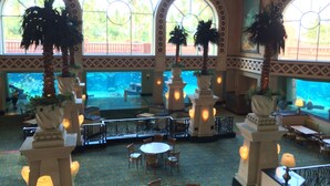 Un atrium intérieur doté de grandes fenêtres en arc de cercle, de palmiers et d’un aquarium.