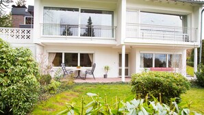 Un edificio de dos pisos con un balcón, un patio con muebles de exterior y un jardín bien cuidado.