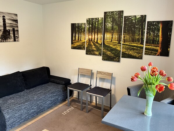 A living room with a black sofa, two chairs, a small table, and a vase of tulips. There are four framed pictures on the wall. - Peace and relaxation near the city of Königswinter (Königswinter)