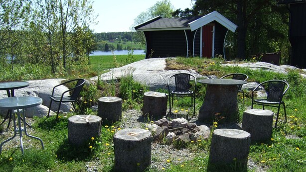 An outdoor seating area with round tables and chairs, surrounded by stone stumps and a fire pit. - Idyllic place for a relaxing holiday (Årjäng)