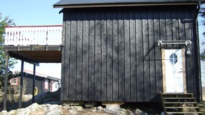 A wooden building with a metal roof, a white door with a window, and a small porch area. - Idyllic place for a relaxing holiday (Årjäng)