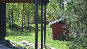 A rustic wooden structure with a metal framework, surrounded by lush greenery and a small red shed. - Idyllic place for a relaxing holiday (Årjäng)