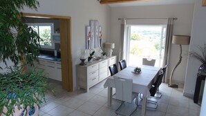 Zona pranzo con tavolo, sedie, un mobile contenitore con oggetti decorativi e vista dalla finestra.