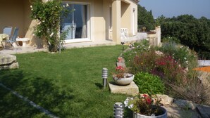 Una casa con patio, prato e diverse piante e fiori in vaso.