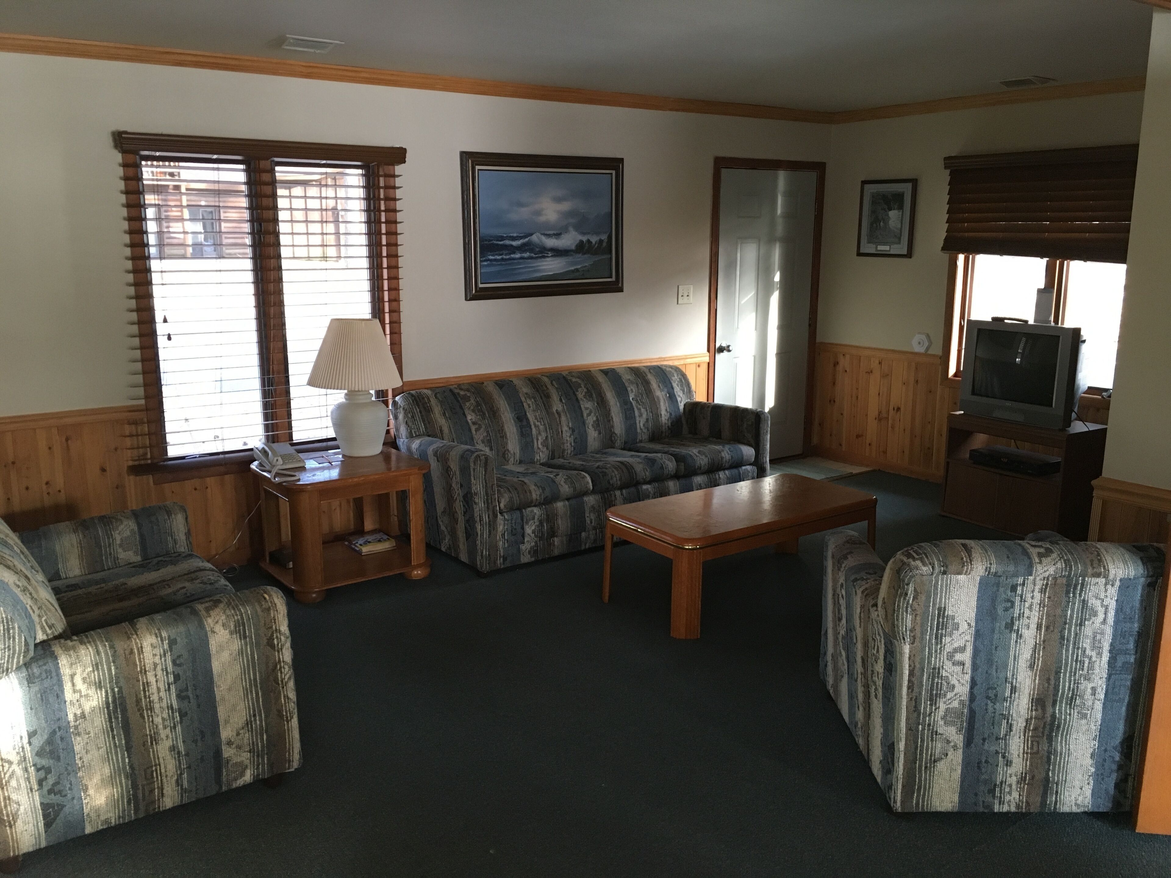 A living room with a sofa, two armchairs, a coffee table, a lamp, and a television.