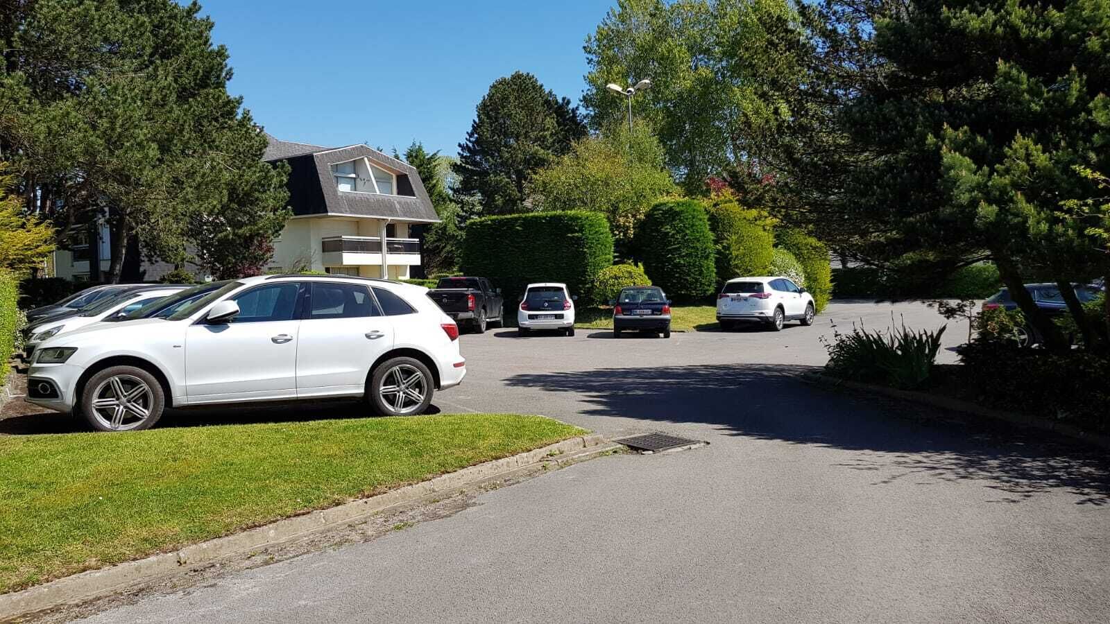 A residential street with parked cars and a house with a sloped roof.