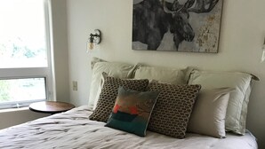 A neatly made bed with a tufted white duvet, two leopard print pillows, and a colorful pillow with a tree design.