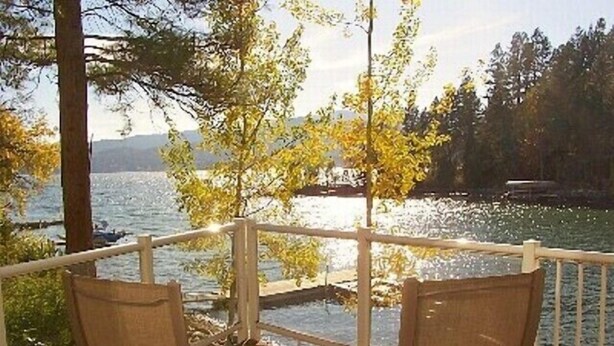 A wooden deck with two wicker chairs facing a lake, surrounded by trees and a railing.