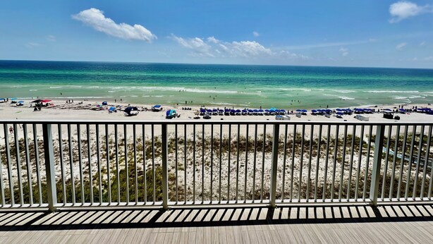 Blick auf einen Strand vom Balkon mit Geländer, feiner Sand und Ozean.