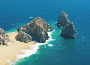 Paisatge costaner amb formacions rocoses i una platja sorrenca.