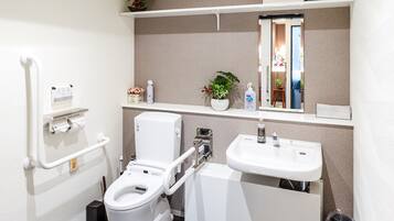 A modern bathroom with a toilet, bidet, and sink, equipped with a handrail and storage shelves.