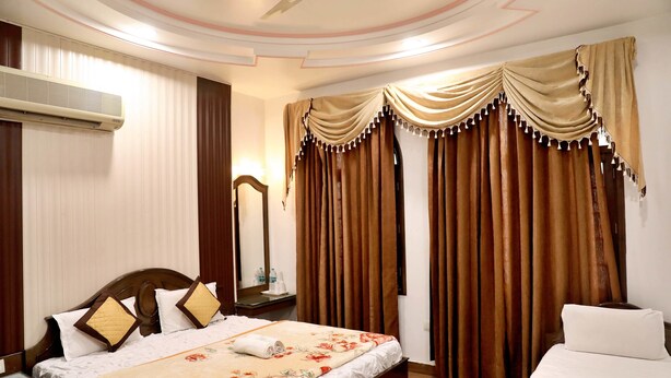 A hotel room with a bed, a nightstand, a mirror, and curtains. - Hotel Heritage Inn (Amritsar)
