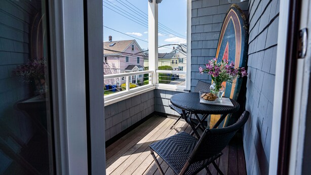 A covered porch with a table and chairs, a surfboard decoration, and a view of neighboring houses. - Downtown Newport Luxury on Thames, 2BR, Sleeps 6 - Walk to Everything (Newport)