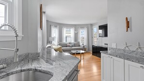 A modern kitchen with granite countertops, a stainless steel sink, and wooden cabinets. - Downtown Newport Luxury on Thames, 2BR, Sleeps 6 - Walk to Everything (Newport)