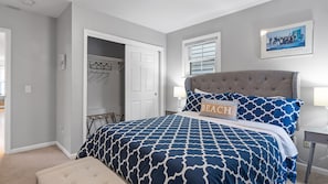 A bedroom with a bed, a nightstand, a chair, a door, and a wall-mounted picture.