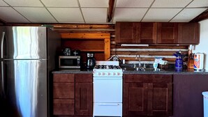 A kitchen with wooden cabinets, a stainless steel refrigerator, a white stove, and a microwave. - Lake Cabin Resort - Cabin 1       (Fife Lake)