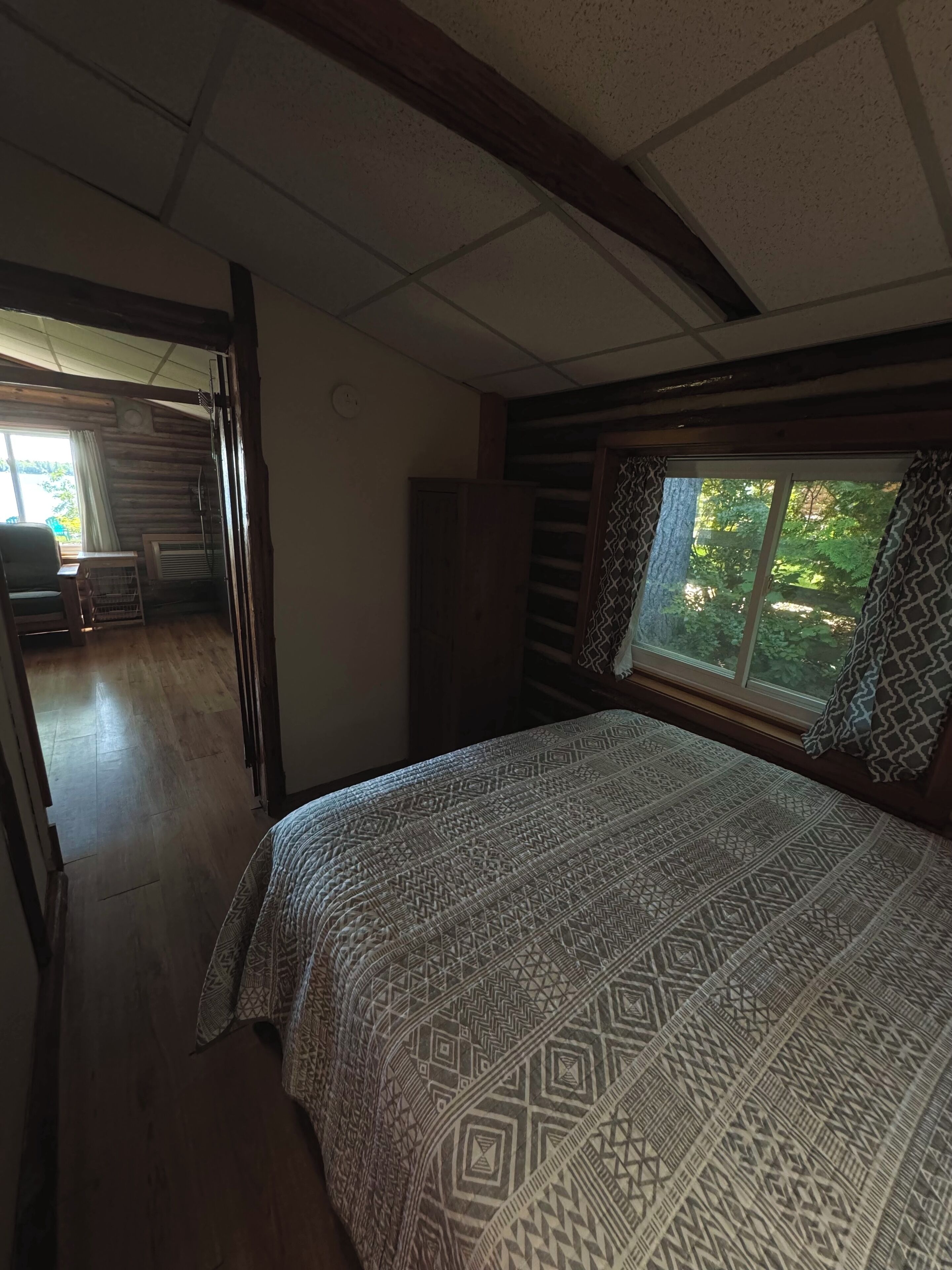 Une chambre avec une couvre-lit à motifs, une fenêtre donnant sur un paysage verdoyant et un plafond en bois.