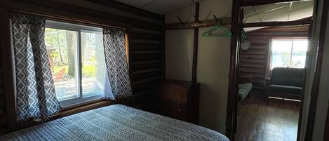 Une chambre à coucher avec un grand lit, des poutres en bois, une commode et une fenêtre ornée de rideaux à motifs.