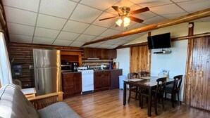 A compact living space with a kitchenette, a dining area, and a sofa. - Lake Cabin Resort - Cabin 1       (Fife Lake)