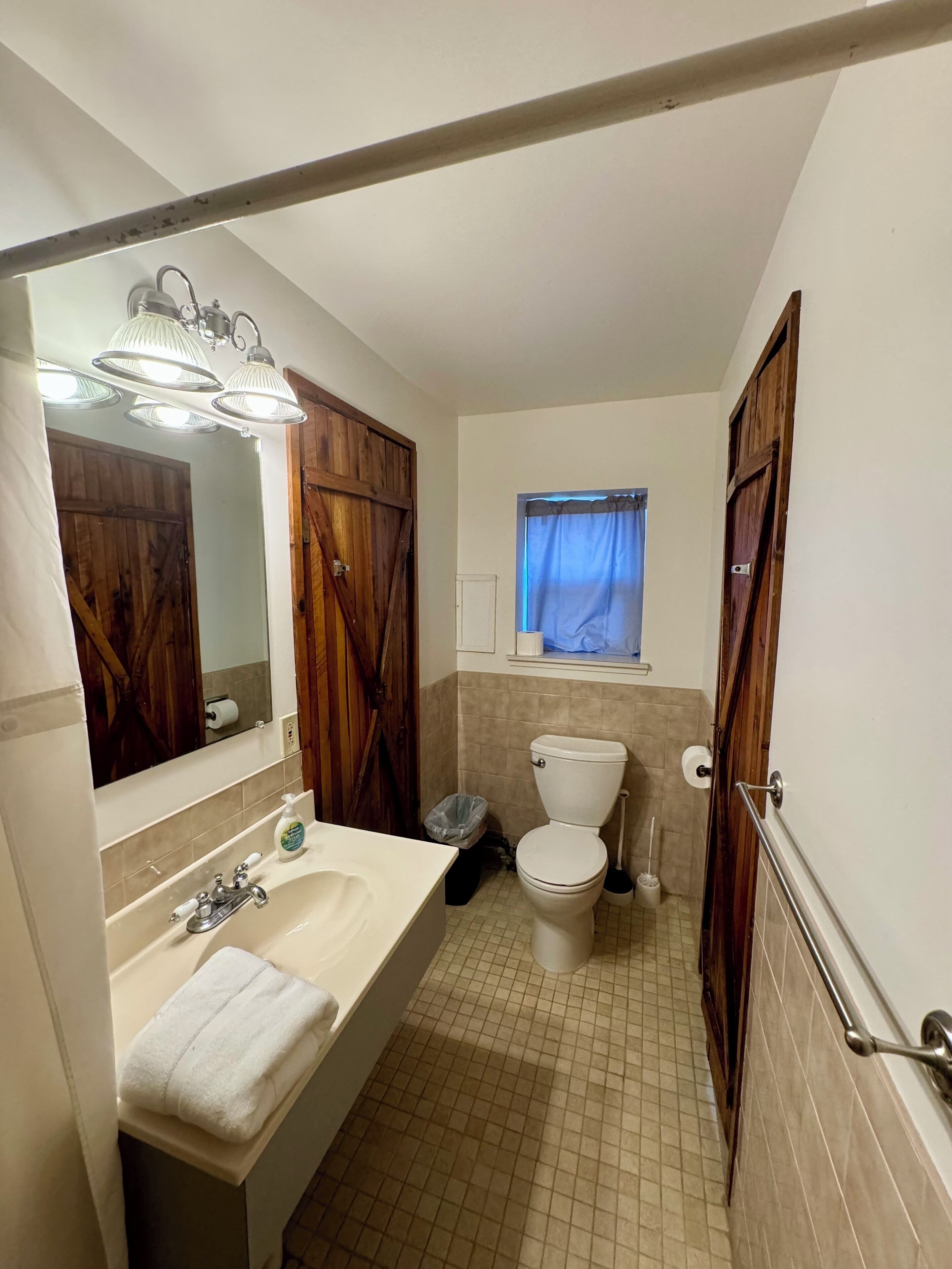 A bathroom with a sink, mirror, toilet, and a window with curtains.