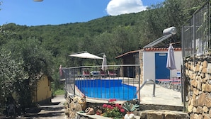 A stone staircase leading to a pool area with a blue pool, surrounded by greenery and a mountain backdrop.