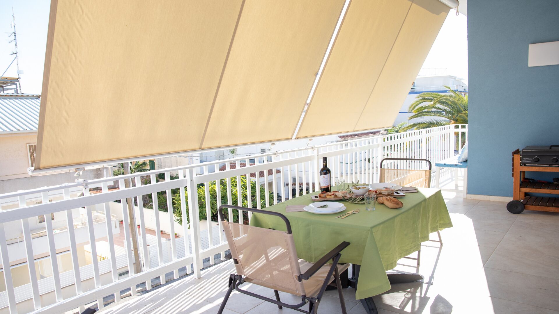 A balcony with a table set for dining, a chair, and a grill cart.