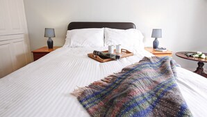 A neatly made bed with white linens, a colorful throw blanket, and a tray with a magazine and two cups. There are two bedside lamps on wooden nightstands. - Eventide - Three Bedroom Cottage, Sleeps 5 (Kingsand)