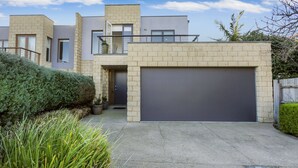 Une maison moderne à deux étages, dotée d’un garage, d’un balcon et d’un jardin bien entretenu.