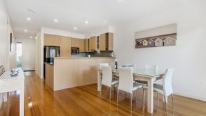 Une cuisine moderne avec des meubles en bois, un îlot central et un coin repas doté de chaises blanches.