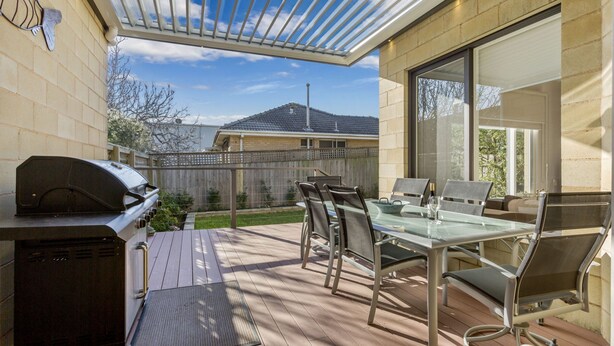 Une terrasse extérieure avec un barbecue, une table en verre et des chaises.