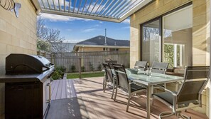 An outdoor patio with a grill, glass table, and chairs. - SUNSET VIEWS - MORNINGTON (MORNINGTON)