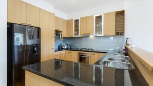 Une cuisine moderne avec des meubles en bois, un réfrigérateur en acier inoxydable, un four à micro-ondes, une cuisinière à gaz et un évier.