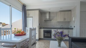 Cozinha moderna com armários brancos, forno embutido e área de refeições com mesa e cadeiras.
