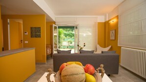 A modern living room with a sofa, a table with fruit, and a view of a garden through a glass door. - Modern, cosy Garden Suite, parking u.r. (Roma)