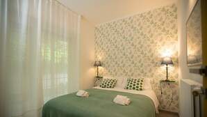 A neatly made bed with a green bedspread and matching pillows, two bedside lamps, and a window with sheer curtains. - Modern, cosy Garden Suite, parking u.r. (Roma)