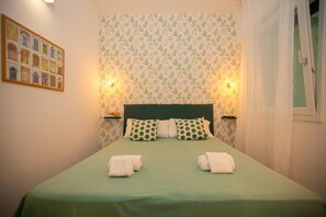 A neatly made bed with green bedding and white pillows, two bedside lamps, and a wall with a floral pattern. - Modern, cosy Garden Suite, parking u.r. (Roma)