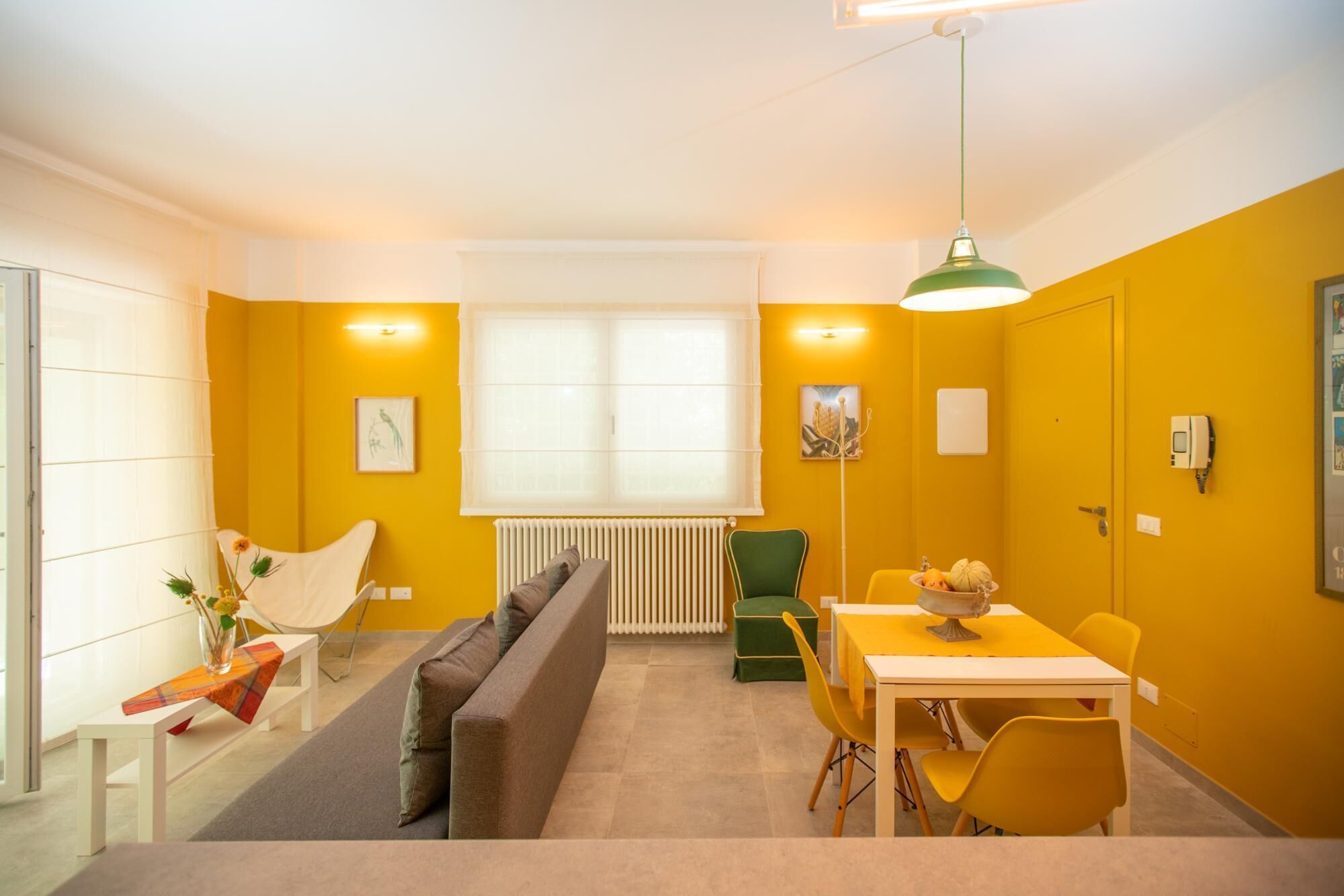 A modern living room with a sofa, a dining table with chairs, a radiator, and a window with blinds.