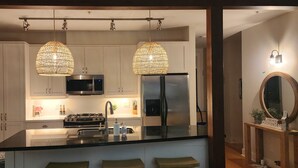 Una cocina moderna con armarios blancos, encimera negra, electrodomésticos de acero inoxidable y dos lámparas colgantes.