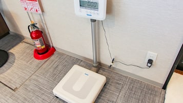 A scale, a fire extinguisher, and a wall-mounted digital device in a room with a carpeted floor.