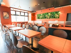 Un intérieur de restaurant moderne avec des tables et des chaises en bois, un mur végétal et une grande fenêtre laissant entrer la lumière naturelle.