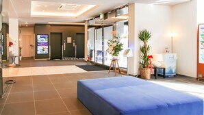 A hotel lobby with a reception desk, a blue seating area, a digital information board, and a plant. - HOTEL LiVEMAX PREMIUM Himejieki-Minami (Himeji)