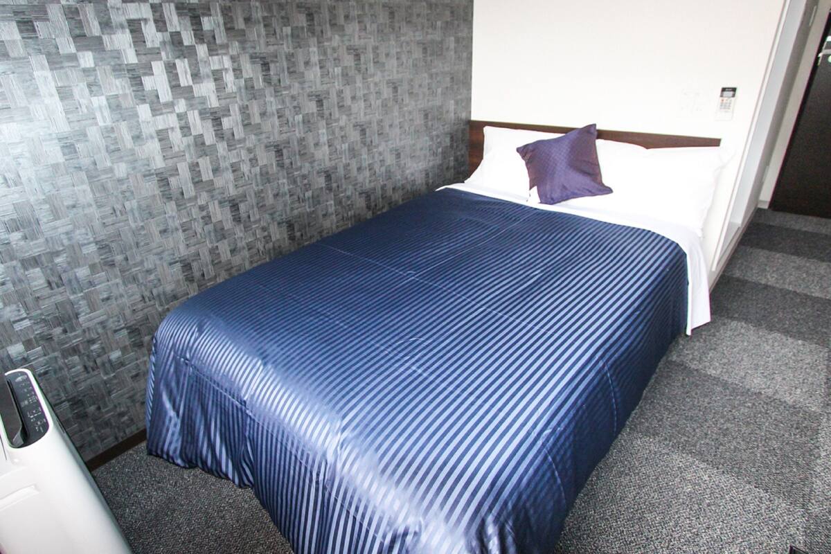 A hotel room with a bed, a textured wall, and a carpeted floor.