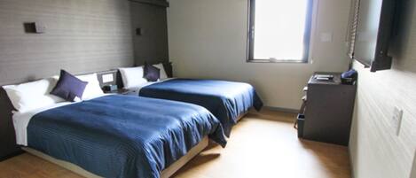A bedroom with two beds, a small desk, a window, and a television.