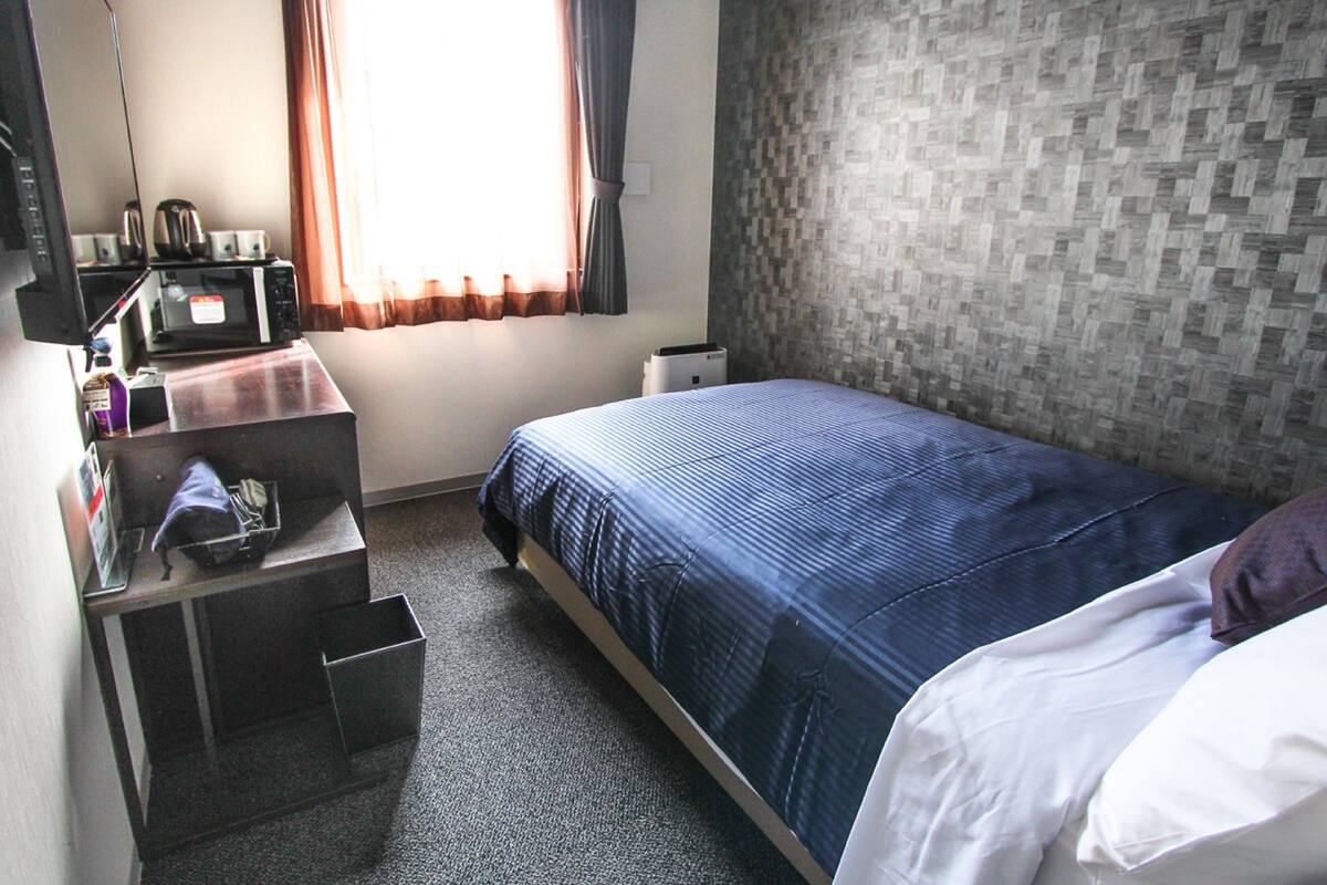 A compact hotel room with a single bed, a desk with a computer, and a microwave.