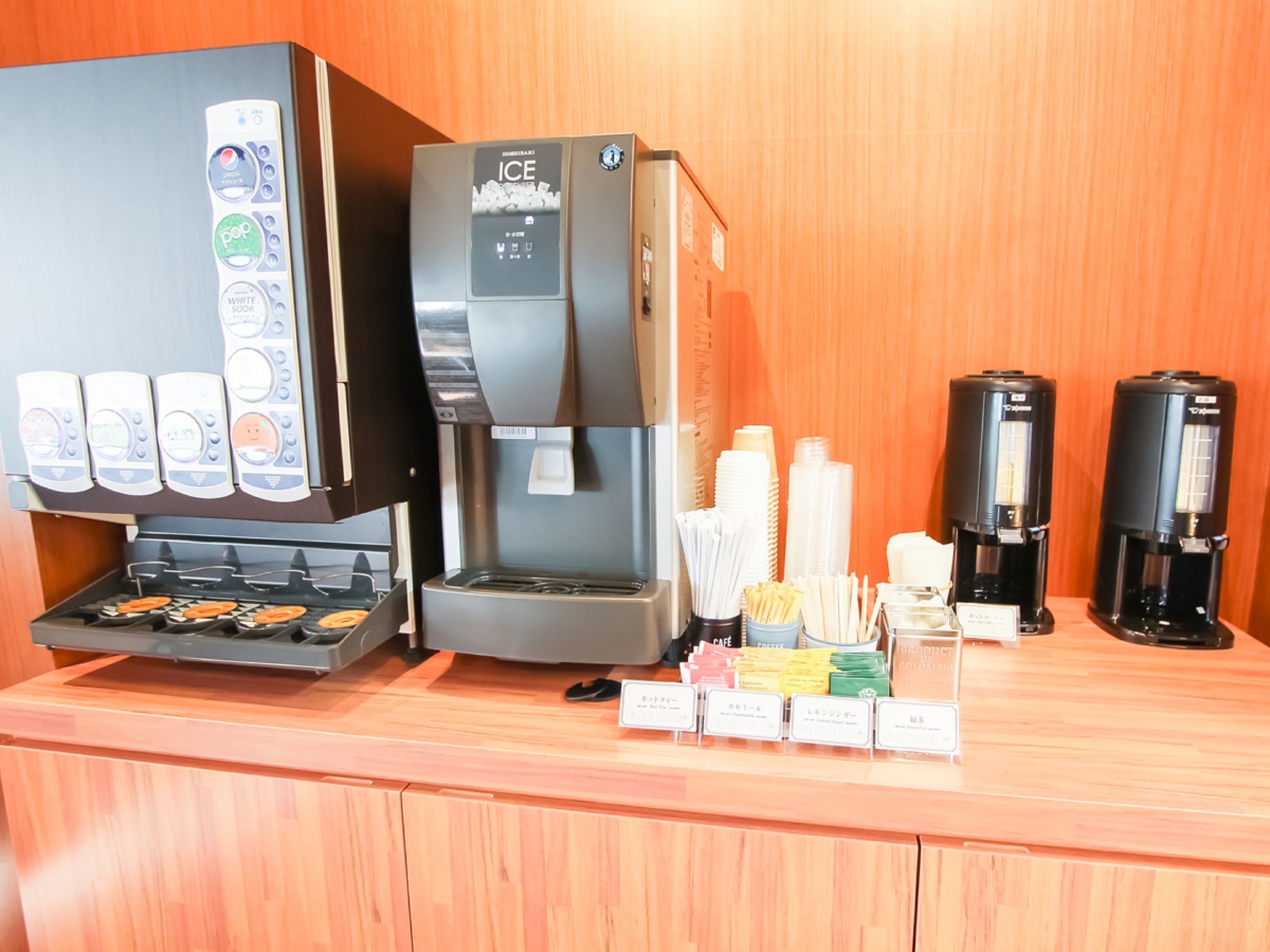 A coffee station with an ice dispenser, a coffee machine, and a variety of disposable cups and utensils.