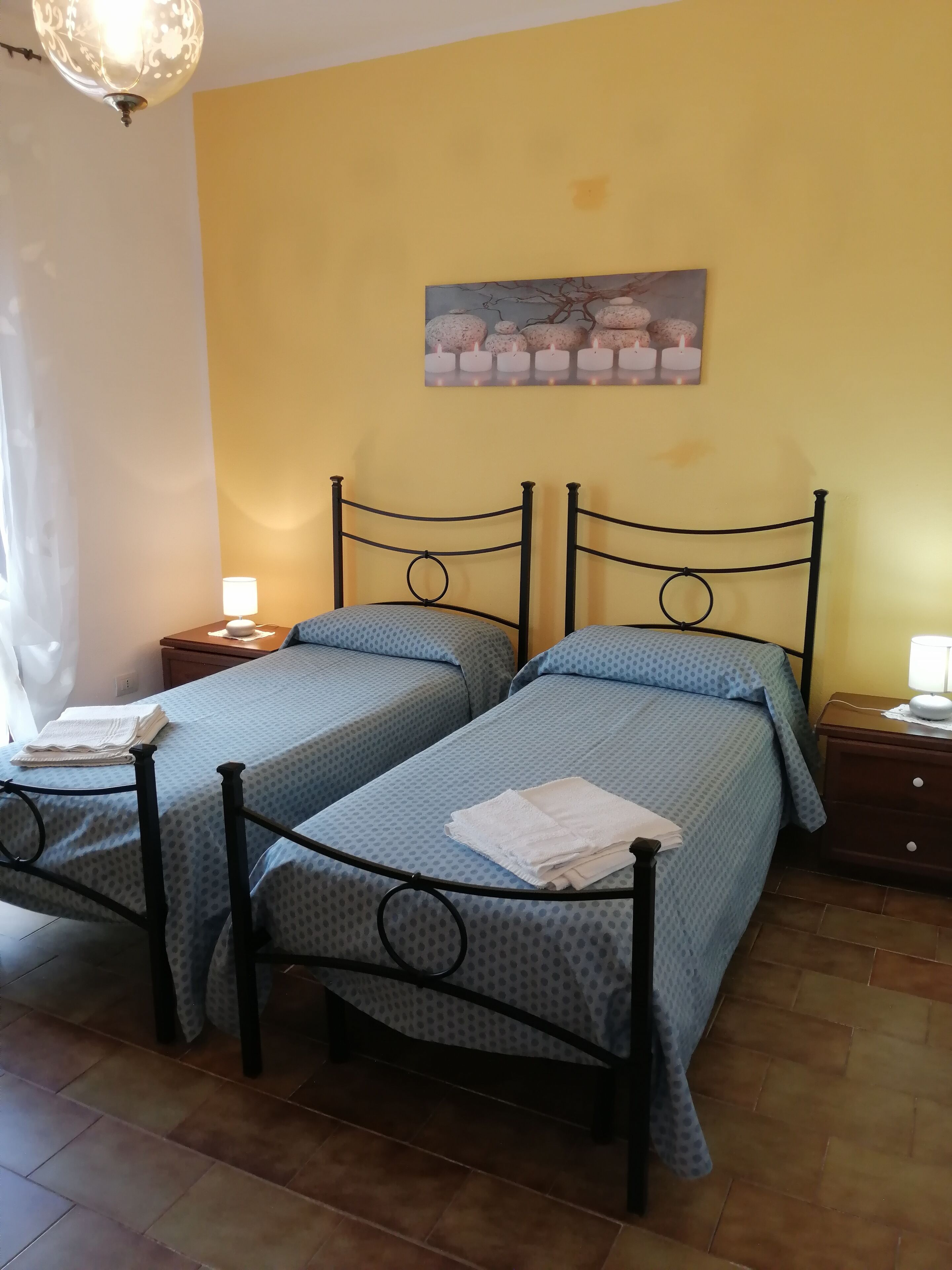 A room with two beds, a painting of candles, and a chandelier.