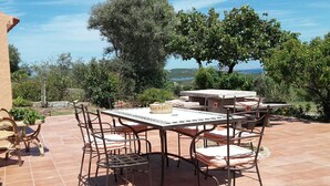Eine Terrasse im Freien mit einem runden Tisch und sechs Stühlen, umgeben von einer Steinmauer und Bäumen.